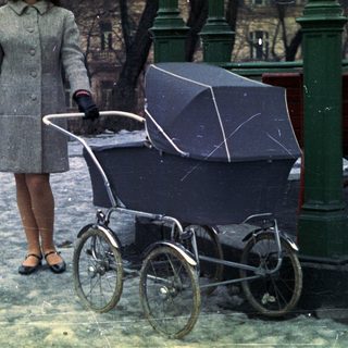 Woman stands near a vintage stroller in a snowy park.
