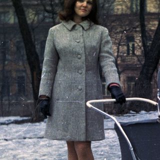 Woman stands near a vintage stroller in a snowy park.