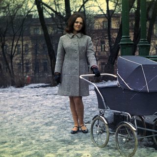 Woman stands near a vintage stroller in a snowy park.