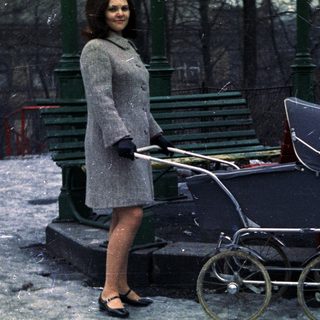 Woman stands in snow, pushing an antique baby carriage.