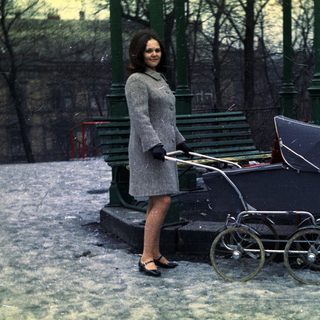 Woman stands in snow, pushing an antique baby carriage.