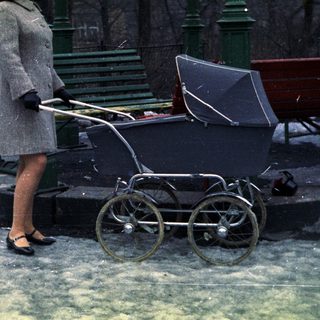 Woman stands in snow, pushing an antique baby carriage.