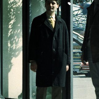 Two men stand near a window, observing a street scene.