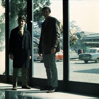 Two men stand near a window, observing a street scene.