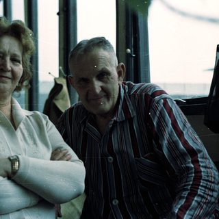 Here's a brief summary of the image: Smiling couple posing for a picture near a window.