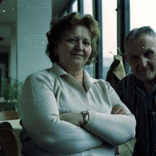 Here's a brief summary of the image: Smiling couple posing for a picture near a window.