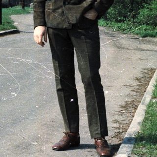Man stands on a road near a building, trees visible.