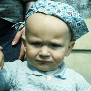 Baby wearing a blue hat and sweater, looking forward.
