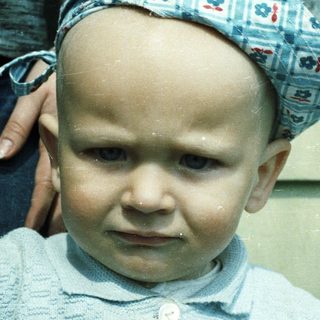 Baby wearing a blue hat and sweater, looking forward.