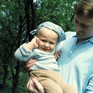 Man holding a baby outdoors in a casual setting.