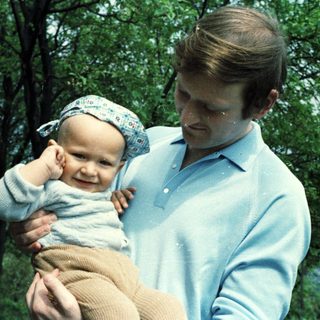 Man holding a baby outdoors in a casual setting.