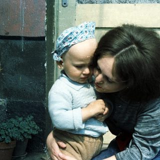 A mother sits holding her baby outdoors.