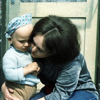 A mother sits holding her baby outdoors.