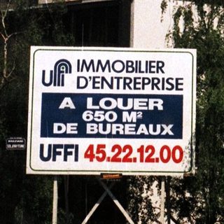 Modern building with signage, palm trees, and a rental advertisement.