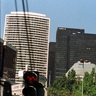 Tall buildings viewed through street signs and traffic lights.