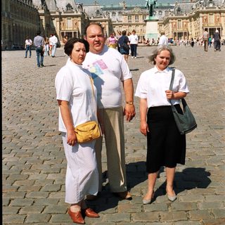Three people stand in front of the Palace of Versailles.