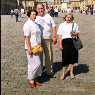 Three people stand in front of the Palace of Versailles.