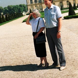 Couple stands in front of a grand palace garden.