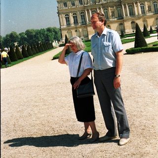Couple stands in front of a grand palace garden.