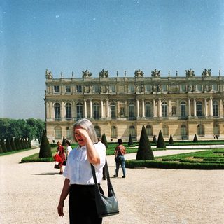 Woman stands in front of the Palace of Versailles.