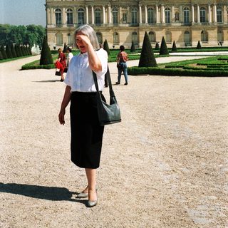 Woman stands in front of the Palace of Versailles.