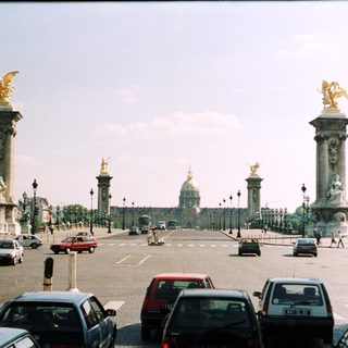 Parisian avenue with monuments, traffic, and a distant dome.