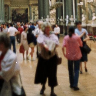 Here's a brief summary of the image: Large museum hall with people viewing artwork and architecture.