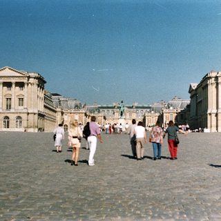 Palace and gardens with people walking in the courtyard.