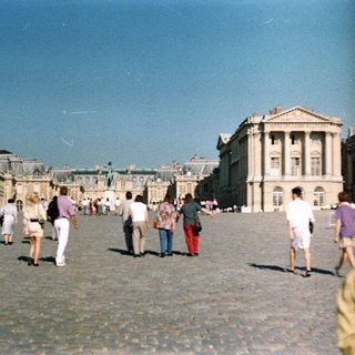 Palace and gardens with people walking in the courtyard.