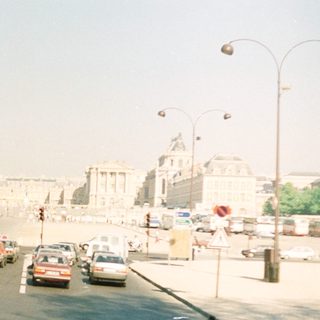 Paris street scene with buildings, cars, and a hazy sky.