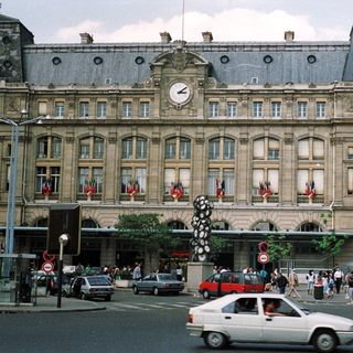 Parisian train station with crowds, cars, and flags.
