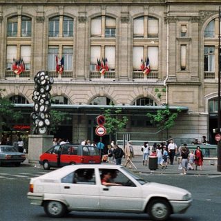 Parisian train station with crowds, cars, and flags.