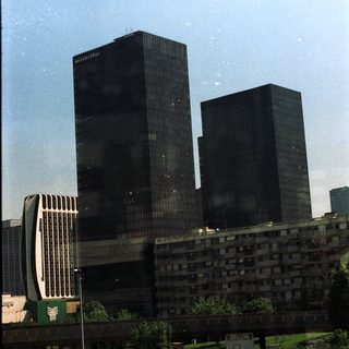 High-rise buildings and surrounding greenery under a bright sky.