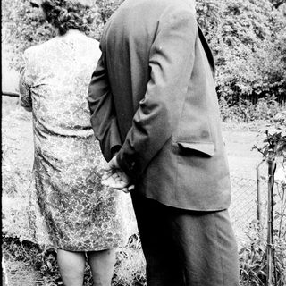 Man and woman standing near a gravesite, looking down.