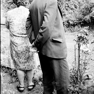 Man and woman standing near a gravesite, looking down.