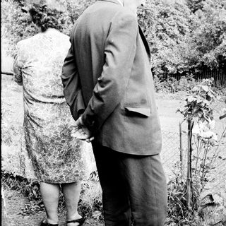 Man and woman standing near a gravesite, looking down.