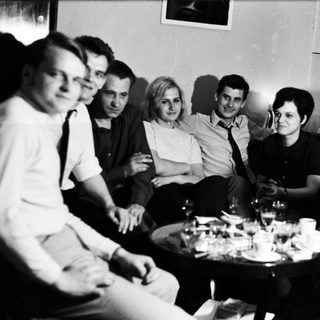 Group of people socializing in a room with a table.