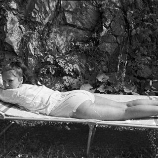 Woman reclines on a bed outdoors, facing the camera.