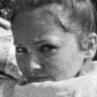 Woman reclines on a bed outdoors, facing the camera.