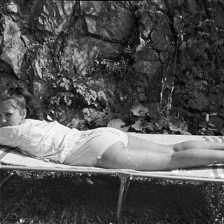 Woman reclines on a bed outdoors, facing the camera.