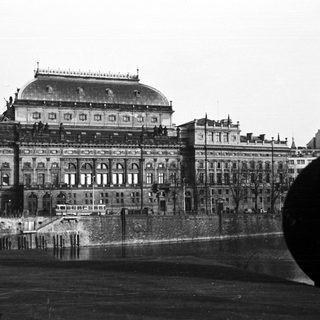 Here's a brief summary of the image: Grand opera house reflected in water, old-fashioned street scene.