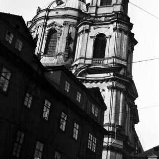 Ornate church tower rises above buildings in a black and white photo.