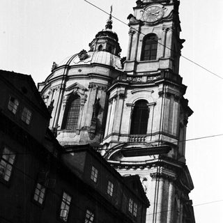 Ornate church tower rises above buildings in a black and white photo.