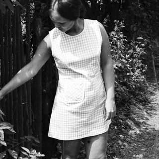 Woman in a checkered dress walks beside a fence.