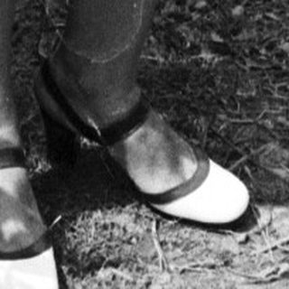 Woman in a checkered dress walks beside a fence.