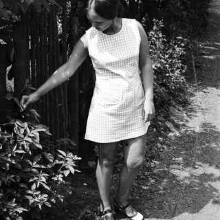 Woman in a checkered dress walks beside a fence.