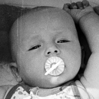Baby in a crib, holding a pacifier.