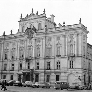 Elegant palace facade with vintage cars and pedestrians visible.