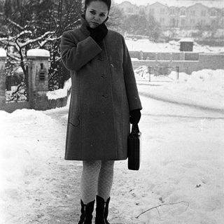 Woman in a coat stands in snowy, wintry landscape.