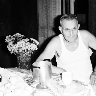 Man seated at a table with eggs and a vase.